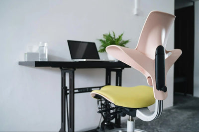 Cadeira ergonômica moderna em escritório com teclado, mouse e notebook na mesa, ambiente de trabalho confortável e organizado.
