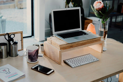 Imagem de mesa de escritório com apoio para notebook, aém de teclado, canecas e livro.