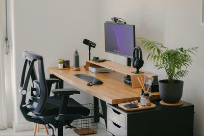 Imagem de escritório com mesa de madeira, notebook, cadeira ergonômica, planta decorativa e itens de escritório.